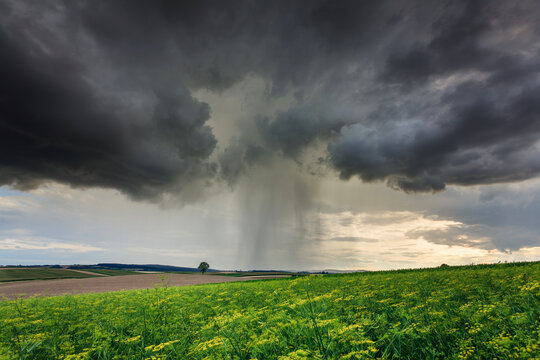 A dark storm cloud and rain over green rural fields.