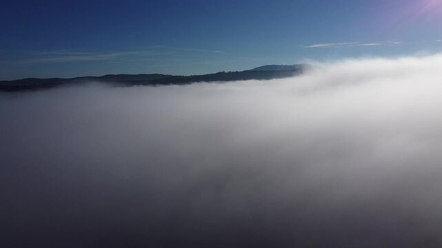 Aerial drone reveal of clouds above planinsko polje in early morning. Drone rises from the foggy level to high above the clouds in the morning