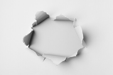 A torn paper hole on a white. The paper is ripped, creating a jagged hole. Torn edges reveal a...