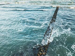 Fototapeta premium Breakwater Extending Into the Sea Surrounded by Waves and Rocky Shoreline at Sunset