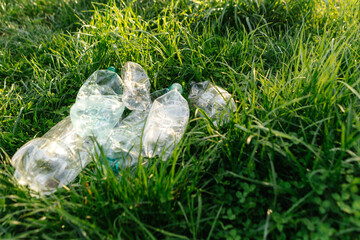 Crumpled plastic bottles are polluting a green meadow, highlighting environmental damage from...