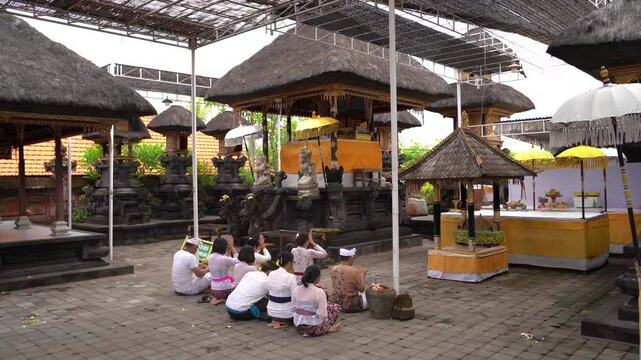Bali, Indonesia : Devotees gather in a serene temple courtyard adorned with colorful parasols for a communal prayer ritual.