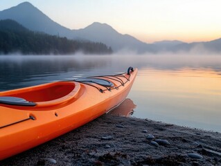 An orange canoe rests on the shore of a serene lake, as the sun sets behind foggy mountains, creating a tranquil scene for adventurers seeking solitude.