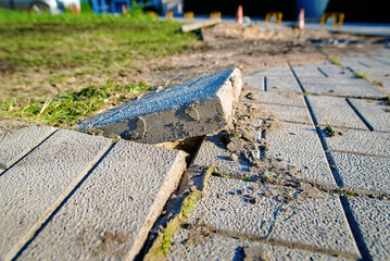 Displaced pavement slabs, cracks, and visible ground erosion.Urban footpath in disrepair with...