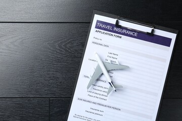 Medical tourism. Travel insurance application form and airplane model on black wooden background,...