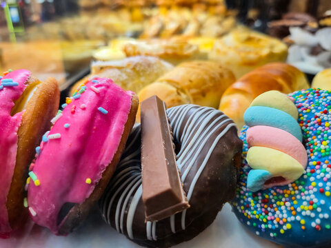 Detalhe de uma estufa de alimentos de uma confeitaria, com v&aacute;rias rosquinhas confeitadas em primeiro plano e salgados variados ao fundo.