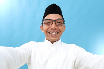 Photo shot of an asian muslim man holding a camera taking a selfie making an excited expression