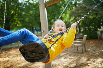Happy 6 years old girl on a swing. Happy kid on playground swinging on seesaw. Outdoor autumn activities for children