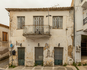 Fototapeta premium abandoned building with balcony and peeling window shutters in Koroni, Peloponnese, Greece