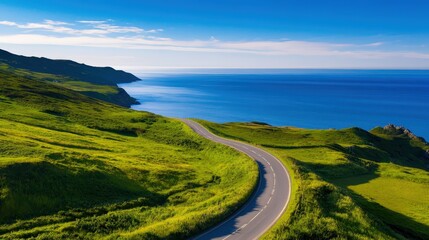 A picturesque coastal road winds through lush green hills, offering stunning views of the vibrant blue ocean under a clear sky, inviting adventure and exploration.