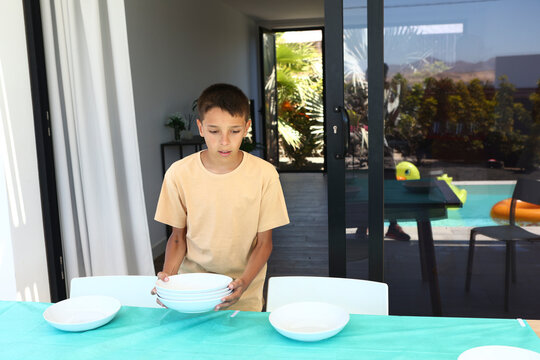Young Boy Setting Table Outdoors by Poolside on Sunny Day