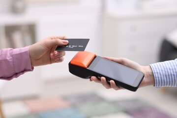 Woman paying with credit card via terminal against blurred background, closeup