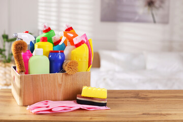Different cleaning products and supplies in box on wooden table indoors, space for text