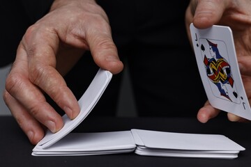 Illusionist shuffling playing cards at black table, closeup