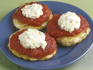 Three breaded chicken cutlets topped with tomato sauce and a dollop of white cheese on a blue plate.