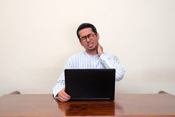 A man suffering back neck pain while sitting infront of a laptop