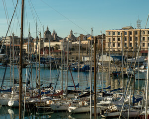 The domes of the city behind the masts of the pleasure boats moored in the main port of Catania