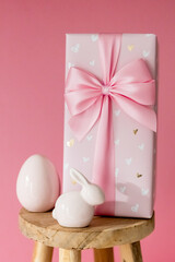 Porcelain Easter egg, bunny, gift box, wooden stool on a pink background.