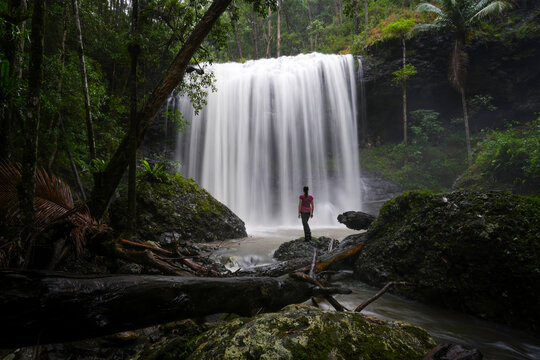 Woman standing at base of waterfall in the rainforest