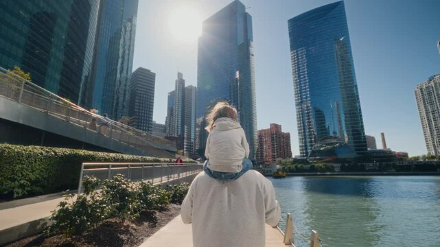 Child is sitting on his father's shoulders as the family walks through a big city with skyscrapers. Slow motion