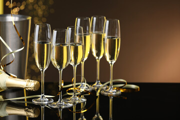 Champagne in glasses and bottle on mirror surface against brown background with blurred lights, space for text