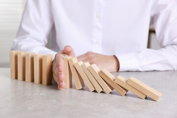 Man stopping wooden blocks from falling at table, closeup. Domino effect