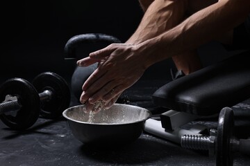 Man applying talcum powder onto his hands above bowl before training in gym, closeup