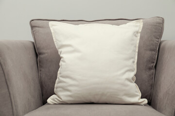Blank soft pillow on cozy armchair against grey background