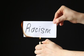 Woman lighting card with word Racism on black background, closeup