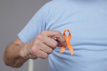 Multiple Sclerosis awareness. Senior man with orange ribbon on grey background, closeup