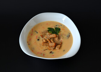 A plate of delicious cheese cream soup with mushrooms and wheat sugars on a black background.