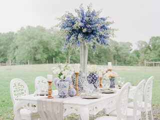 Outdoor dining setup featuring elegant floral arrangements and delicate tableware in a serene countryside setting