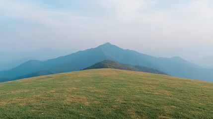 Fototapeta premium Serene mountain landscape with rolling green hills and distant peaks under a blue sky.
