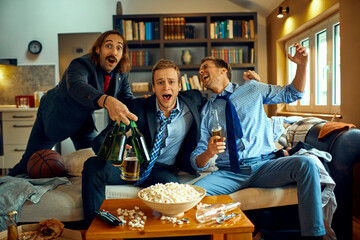 Young group of people watching a basketball game on the tv in the living room while having beer and...