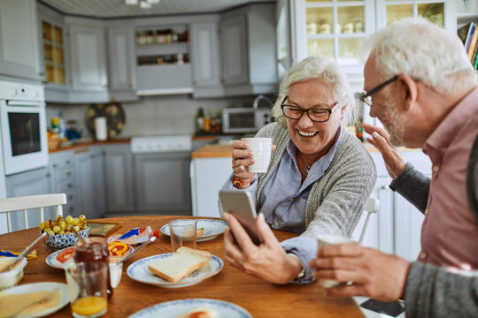 Happy senior couple using smartphone at breakfast in cozy kitchen