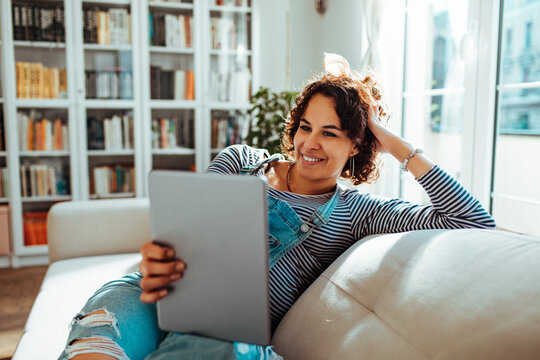 Smiling woman relaxing on couch using tablet at home