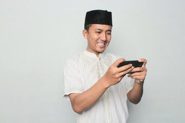Asian Muslim man is playing with a smartphone with a white background.