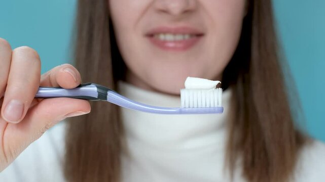 Young woman squeezing toothpaste on toothbrush on blue background.