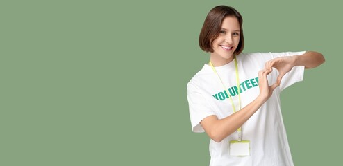 Young female volunteer making heart with her hands on green background with space for text