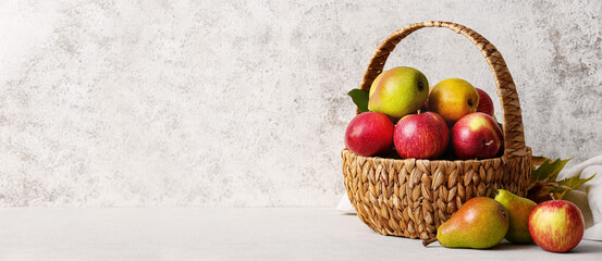 Basket with ripe pears and apples on light background