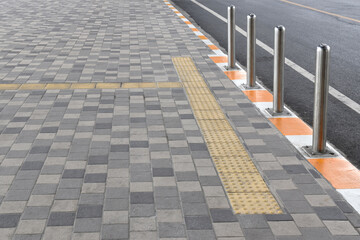 Obraz premium silver stainless steel pole barrier on curb with direction braille block tile on gray tile pavement, safety post protection and rough tactile tile for guidance visually impaired person