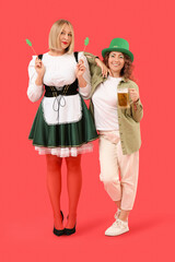 Portrait of women with beer celebrating St. Patrick's Day on red background