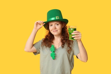 Young redhead woman in hat with beer on yellow background. St. Patrick's Day celebration