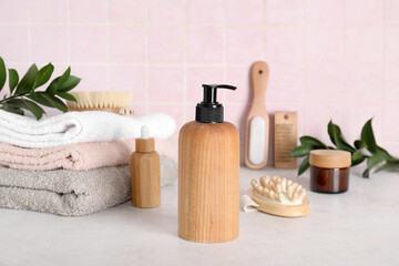 Composition with shampoo, massage body brush and towels on grey table near pink tile wall