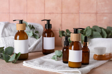 Composition with bottles of shampoo, towels and green twigs on light table near pink tile wall