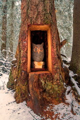 wooden sculpture of a smart owl in a large spruce tree trunk in a winter forest