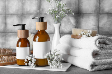Composition with bottles of shampoo, flowers and towels on table near grey grunge tile wall