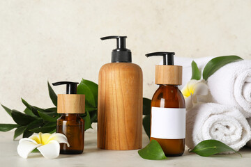 Composition with bottles of shampoo, towels and flowers on table near beige grunge wall