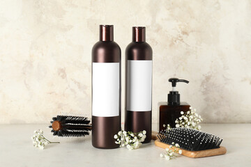 Composition with bottles of shampoo, hair brushes and flowers on table near beige grunge wall