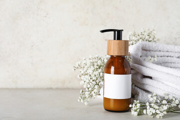 Composition with bottle of shampoo, towel and flowers on table near beige grunge wall, closeup